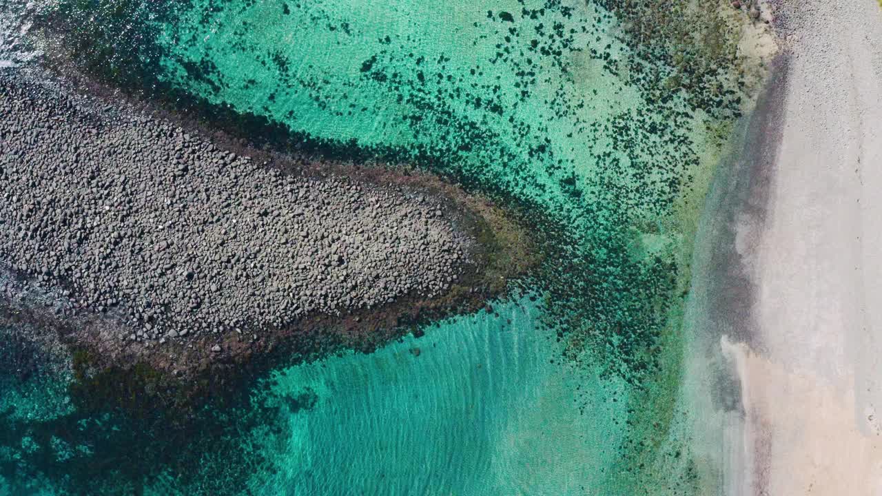 美丽的水晶般清澈的浅水环绕着沙滩上的岩石露头。视频下载