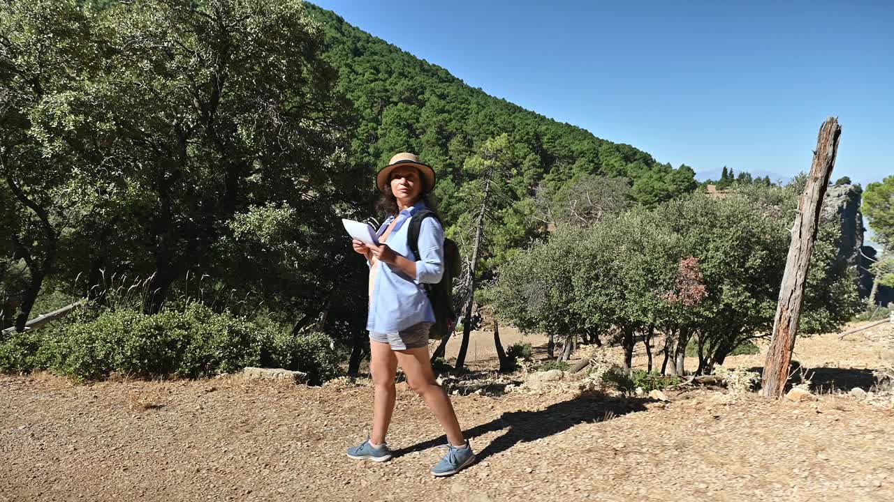 一名女子在阳光明媚的大自然小径上徒步旅行，手持地图，在宁静的森林环境中进行户外冒险。视频素材