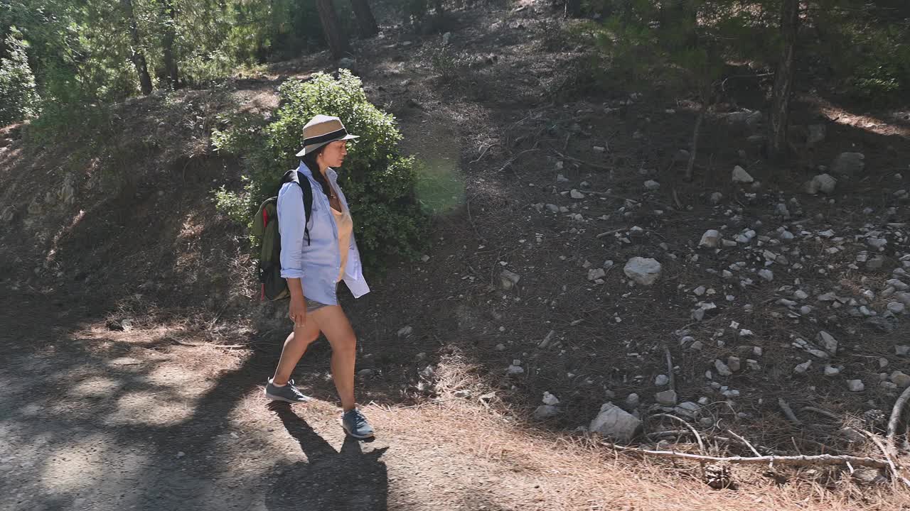 一名女子背着背包，戴着帽子，徒步穿过森林中布满岩石的小径，享受户外冒险和自然探索视频素材