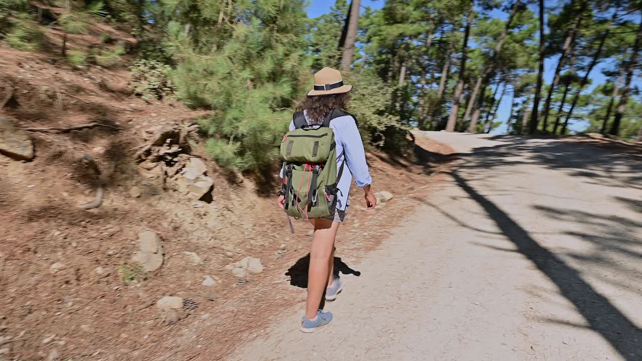 在阳光明媚的日子里，年轻女子在风景秀丽的森林小径上徒步旅行，享受大自然的美丽和户外冒险视频素材