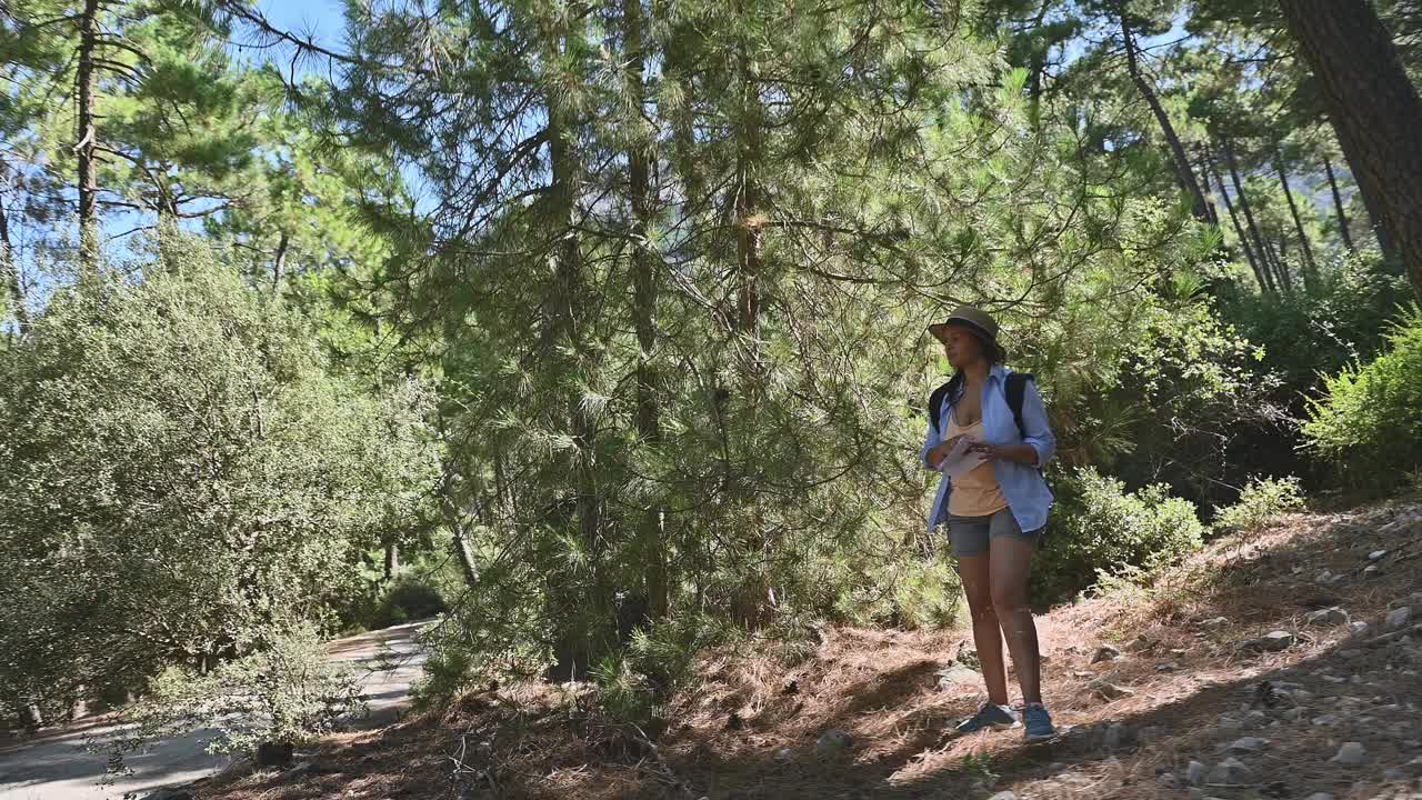 一个女人在一个阳光明媚的日子里在郁郁葱葱的森林里徒步旅行，享受大自然和户外冒险，戴着帽子，背着背包视频素材