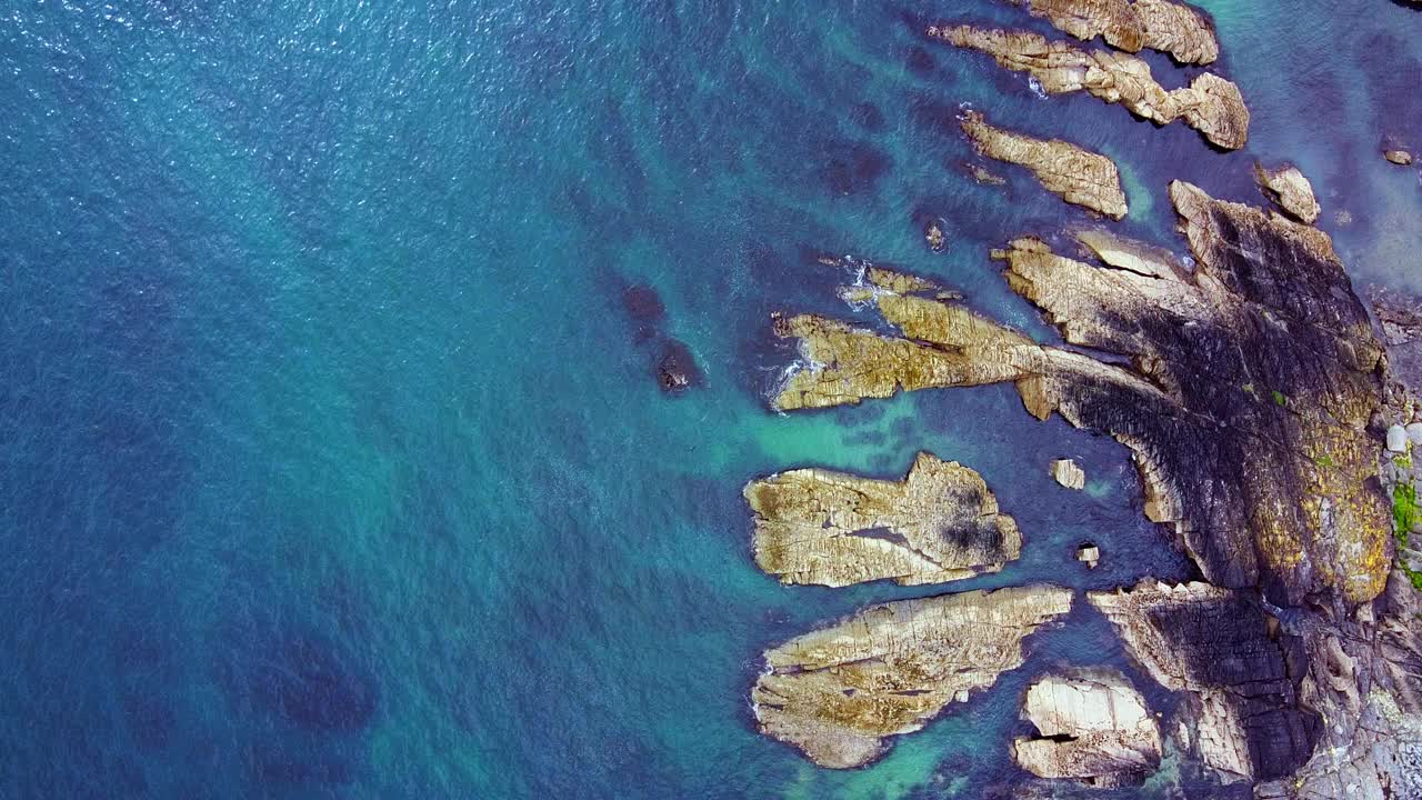 这是一段航拍视频，拍摄了崎岖的海岸线，有不同的岩层和蓝绿色的海洋。视频下载