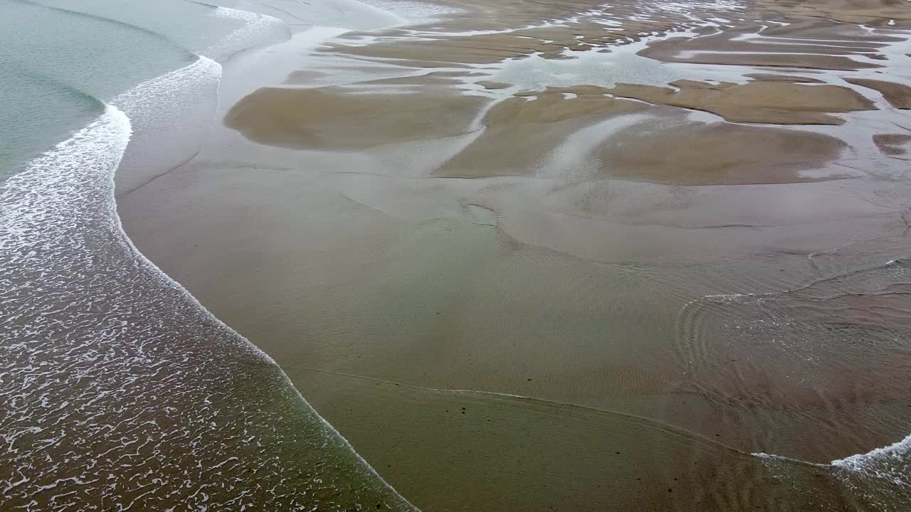 沙滩鸟瞰图，后退的海水揭示了复杂的沙洲和河道。水面平静而浅，反射出淡蓝色的天空。视频下载