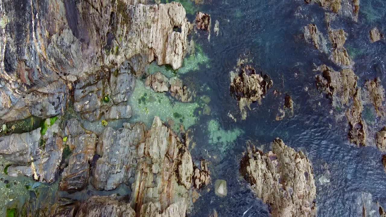 沐浴在阳光下的岩石海岸线全景，海洋在蓝色和绿色的阴影下闪闪发光。视频素材