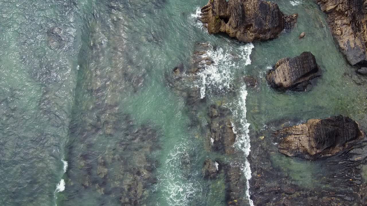 从鸟瞰角度看，崎岖的岩石突出到充满活力的绿松石海中。视频素材