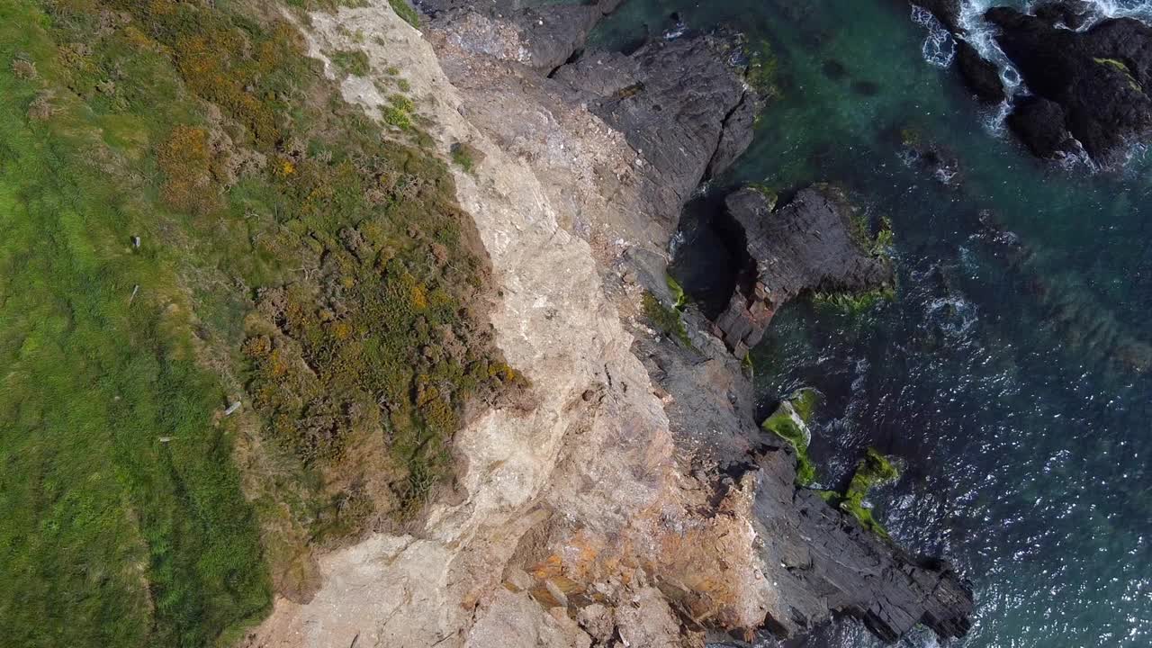 从岩石海岸线上俯瞰的景色。深灰色的岩石与蓝绿色的海水和白色的浪花形成鲜明的对比。海水足够清澈，可以看到海底，露出沙子和海藻的混合物。视频下载