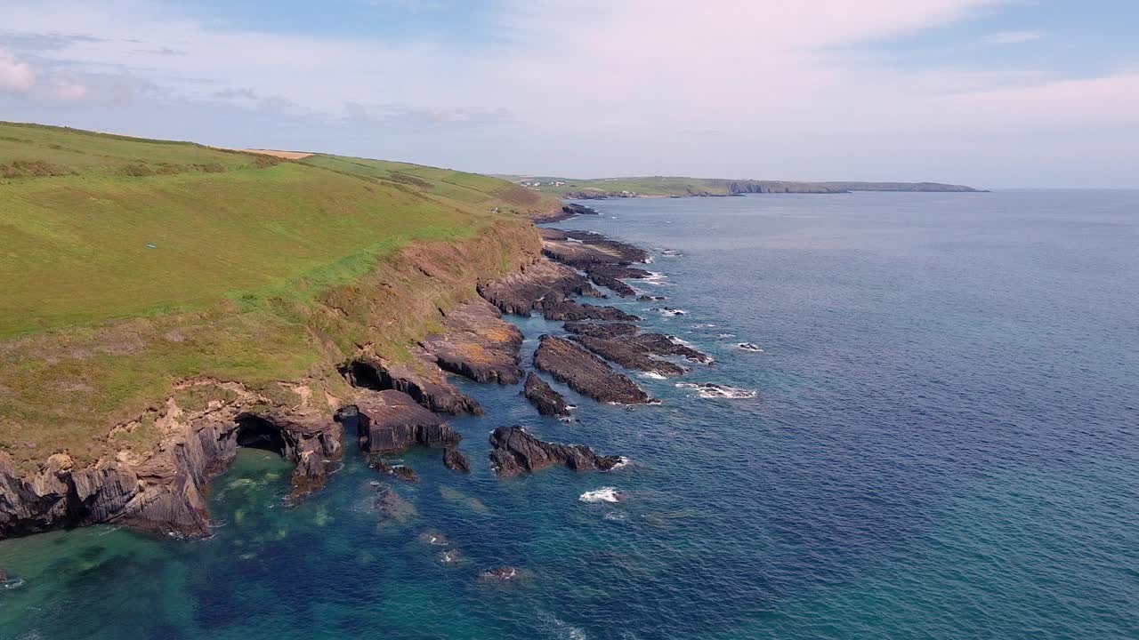 岩石嶙峋的海岸线，山顶是长满绿草的小山。水是湛蓝的，天空是多云的。视频下载