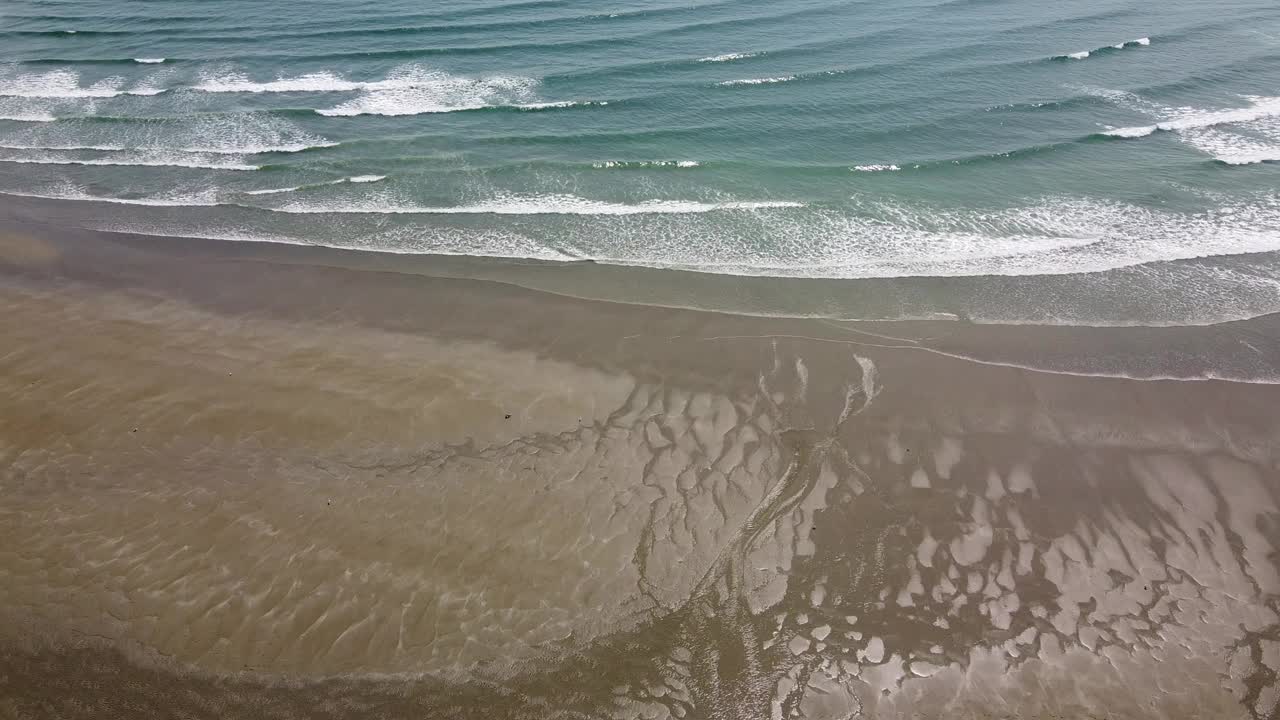 平行的海浪拍打着海岸，在蓝色的海水上形成了重复的白色泡沫。视频素材