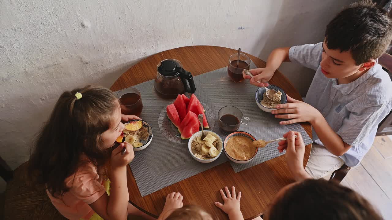 孩子们在舒适的桌子旁享受着健康的早餐，有燕麦片、水果和茶，在家里创造了一个温暖而诱人的氛围。视频素材