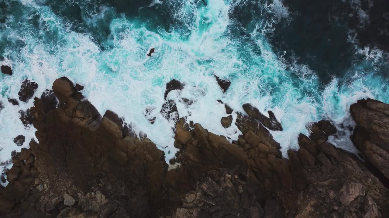 从空中拍摄的美丽的绿松石海浪冲击着岩石悬崖。视频下载