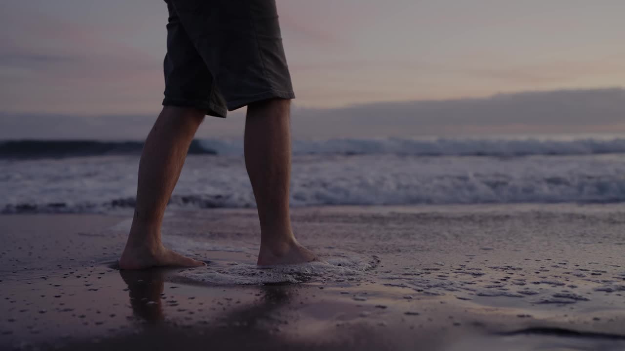 一名男子在宁静的日落中赤脚走在海滩上视频素材