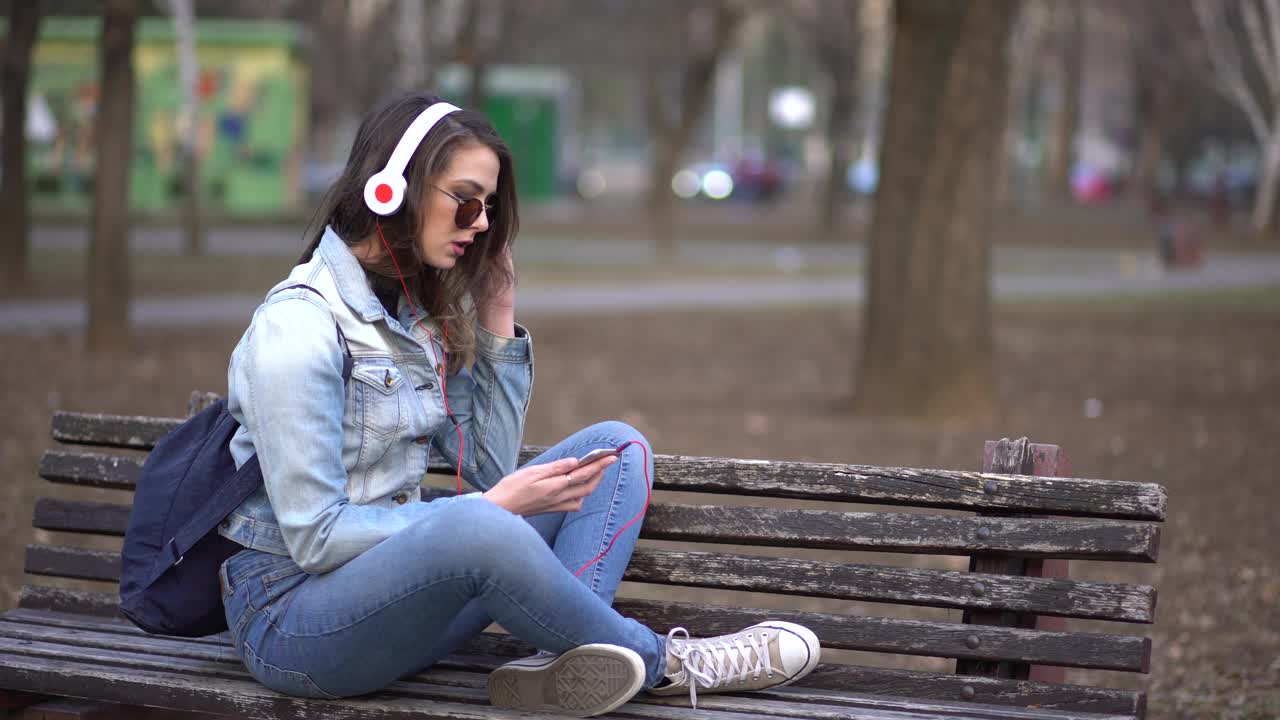 一位年轻女子坐在公园的长椅上听音乐视频素材