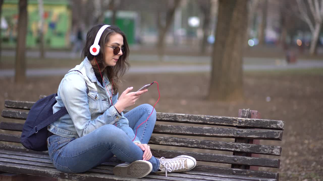 一位年轻女子坐在公园的长椅上听音乐，用手机打电话视频素材