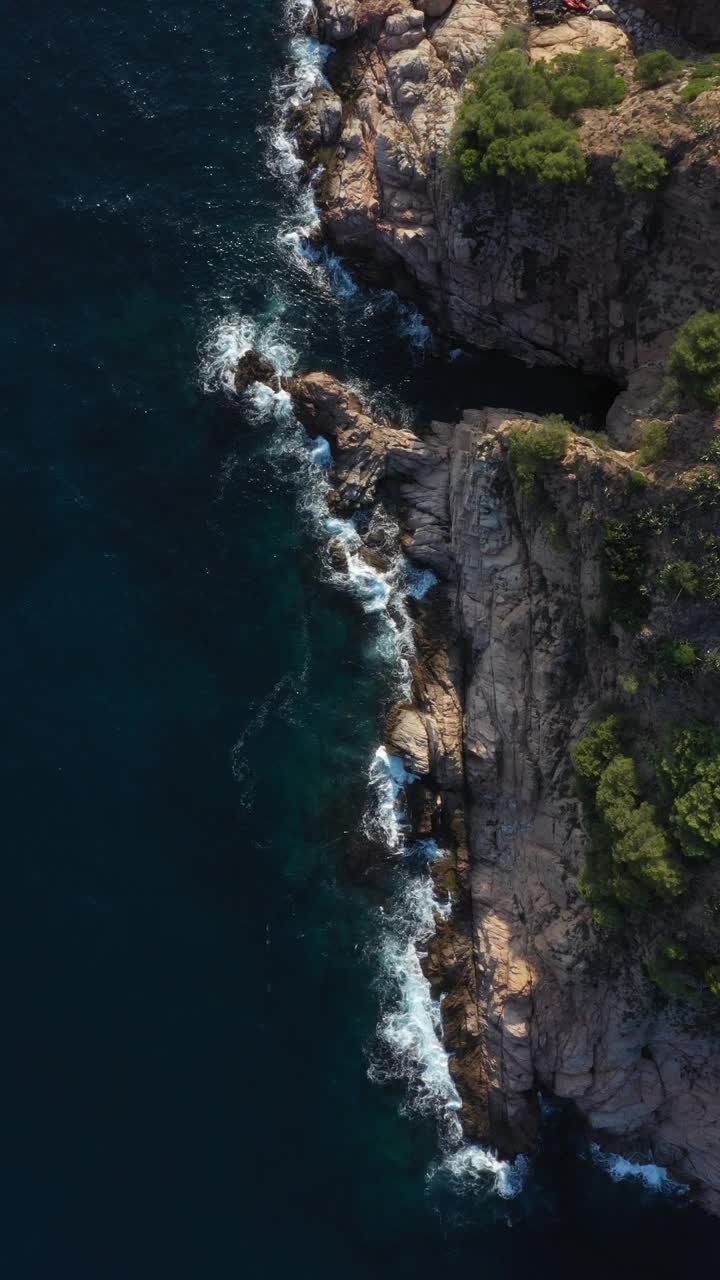 空中垂直视频。海浪撞击岩石的俯视图。视频下载