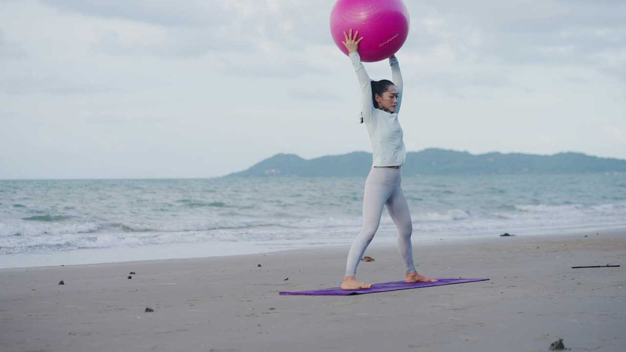 老年妇女早上在沙滩上健身球伸展运动。视频素材