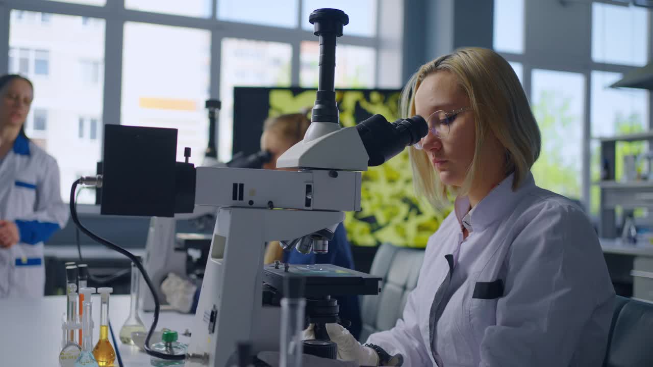 聪明的女学生在化学教室里透过显微镜看，学校里的肖像视频下载