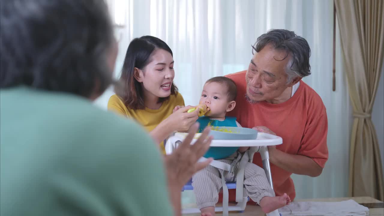 一个小孩吃了他的第一顿饭，父母和祖父母兴奋地欢呼视频素材