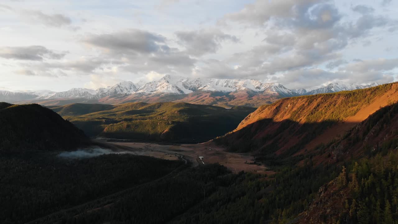 与雪山相对的丘陵地带。金色的夕阳照亮了自然景观视频下载