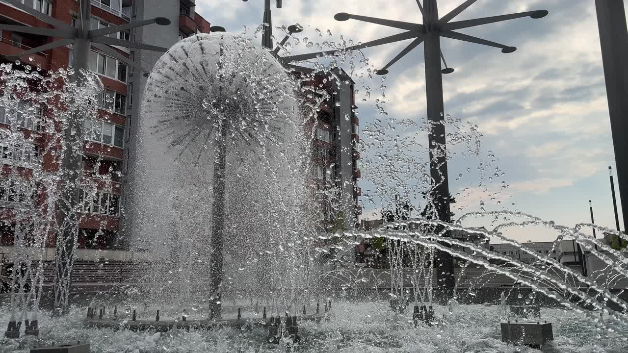 近景:喷泉的水流流入室外的池塘，蓝色的多云的天空和建筑物为背景视频下载