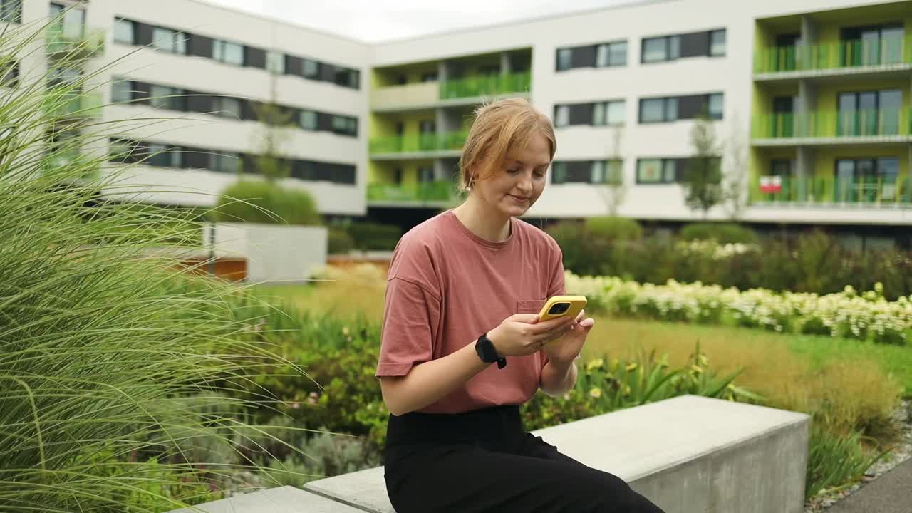 漂亮漂亮的金发年轻女子在城市街道背景的智能手机上发短信。视频素材