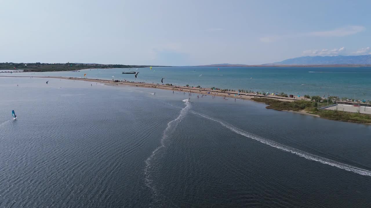 在克罗地亚尼恩市的兹德里亚克海滩，无人机拍摄的风筝冲浪者的航拍照片。游客在兹德里亚克沙滩和亚得里亚海放松，背景是狄纳里阿尔卑斯山脉视频下载