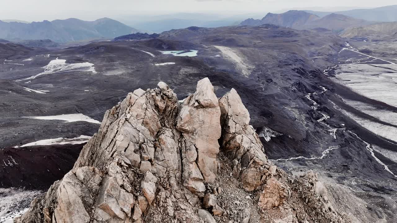 陡峭的山峰是一座古老的岩石山，高耸在布满火山岩和冰川的死气沉沉的田野上。鸟瞰图视频下载