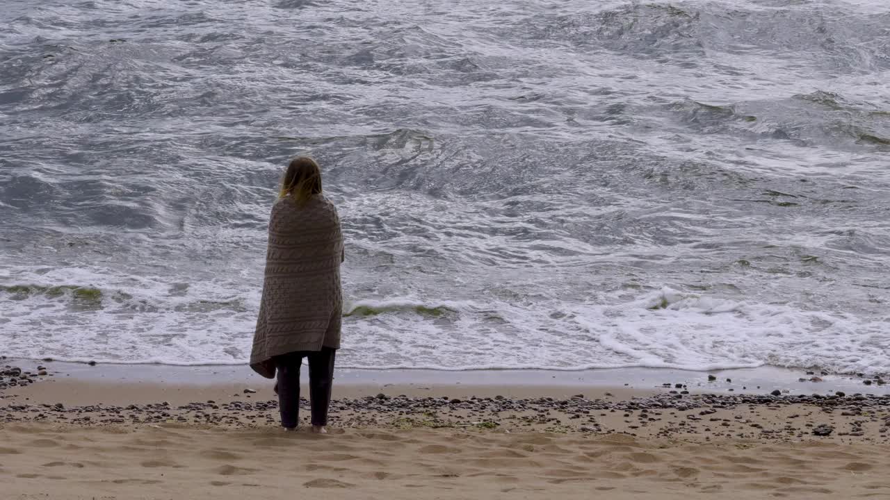 女人站在沙滩上，面对着巨大的海浪视频下载