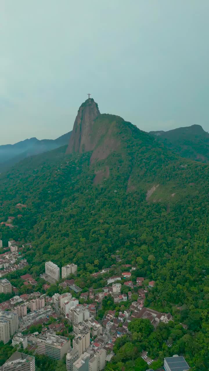 鸟瞰图里约热内卢的救世主基督雕像在科尔科瓦多山上，周围是郁郁葱葱的绿色植物和城市景观。视频下载