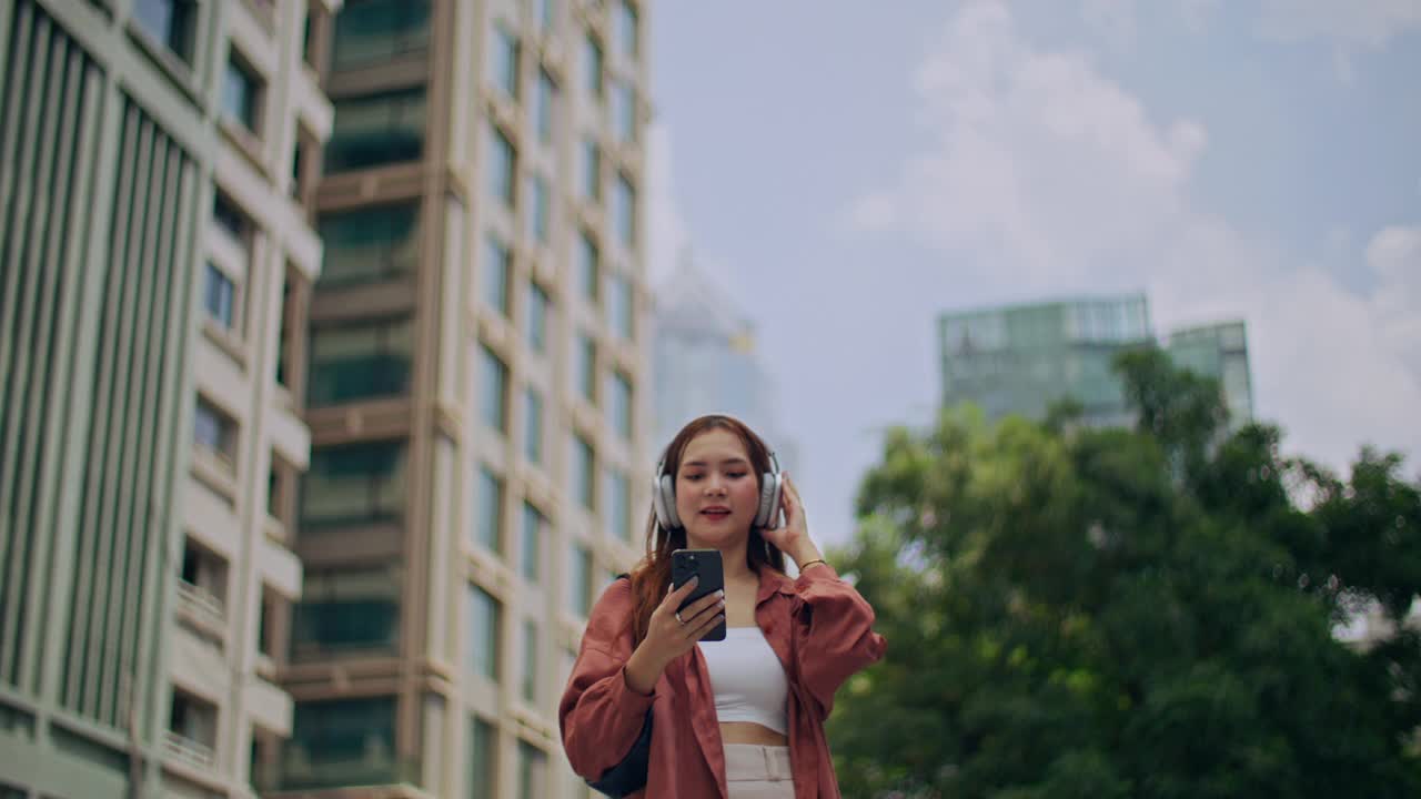 亚洲女人用耳机听好听的音乐，站在城市里视频素材