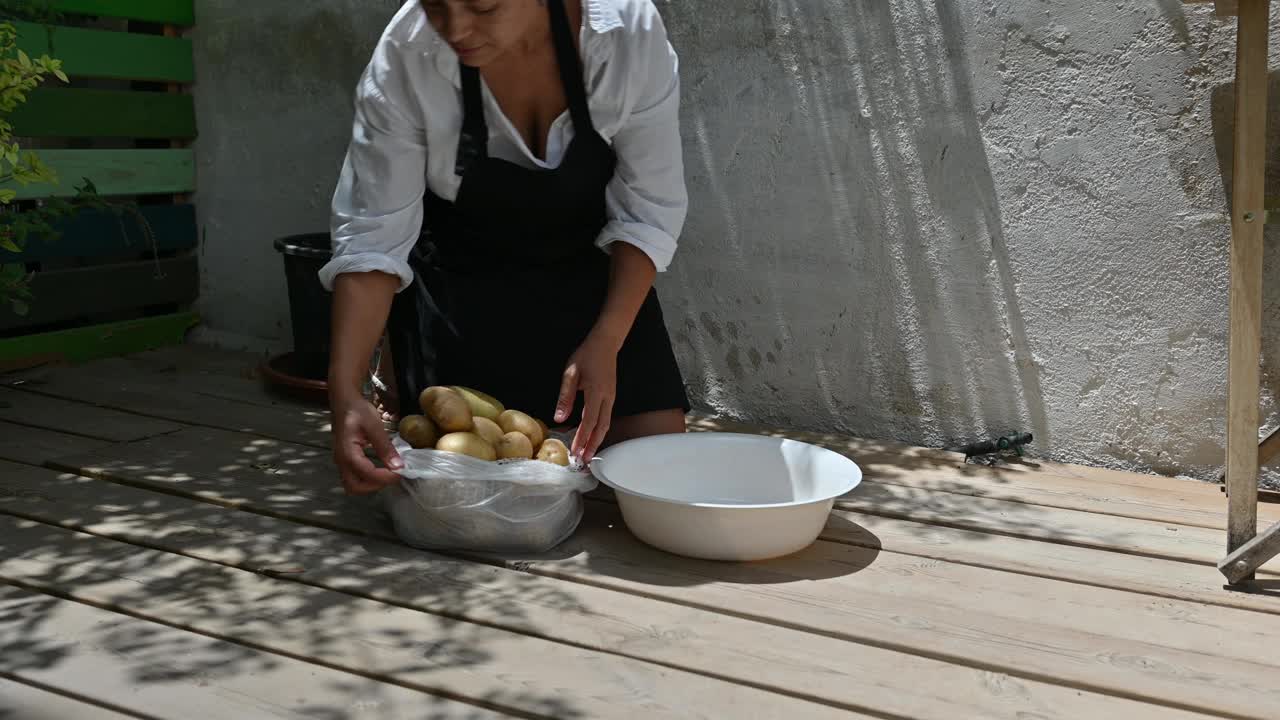 一名妇女在乡村的户外环境中为瓦列尼基准备土豆，展示了传统烹饪和家常菜的制作，阳光在木地板上投下阴影。视频素材