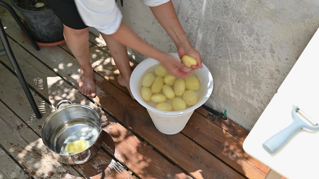 一名妇女在木甲板上用桶洗土豆，在自然光下捕捉烹饪准备的瞬间视频素材