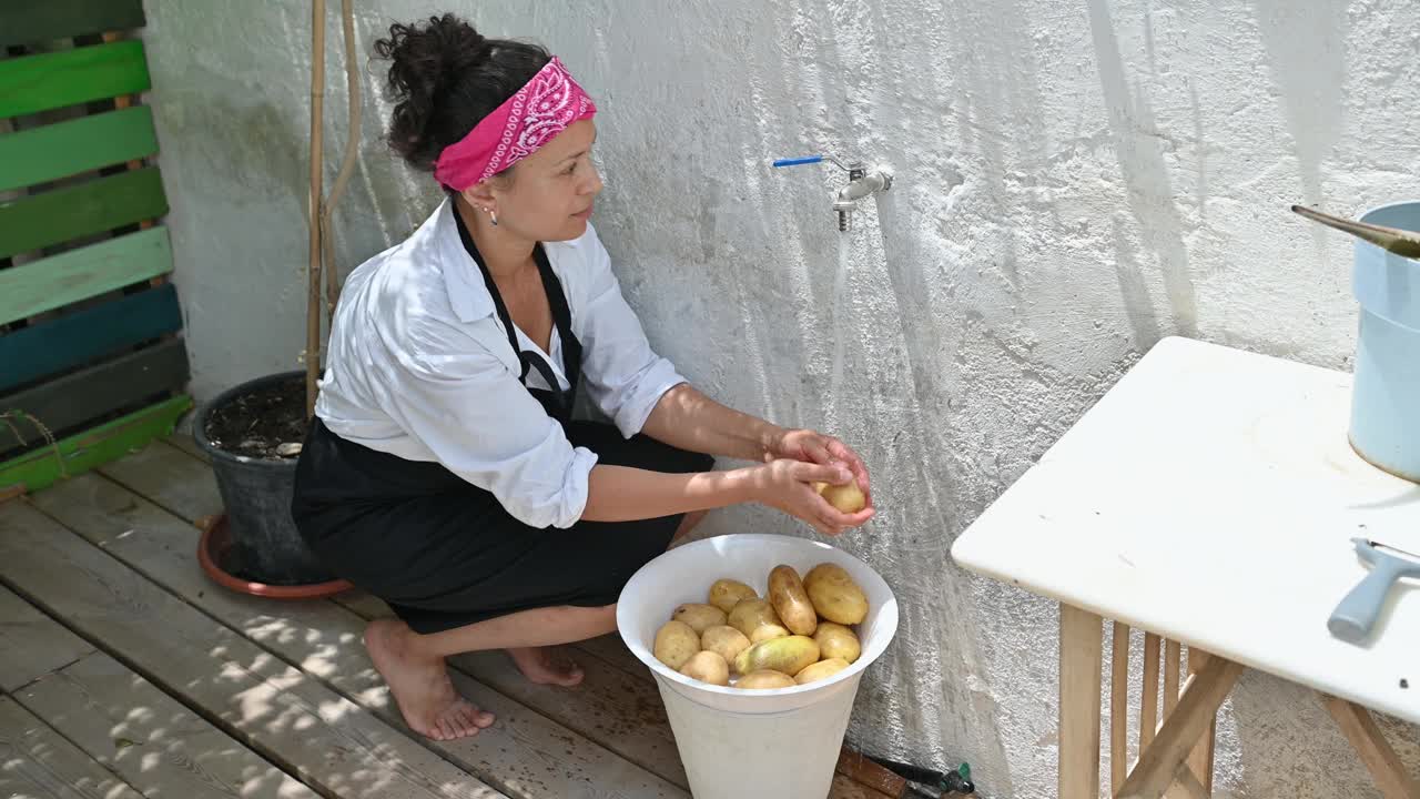 一名妇女在户外的水桶里洗土豆，在乡村的环境中准备自制烹饪的食材视频素材