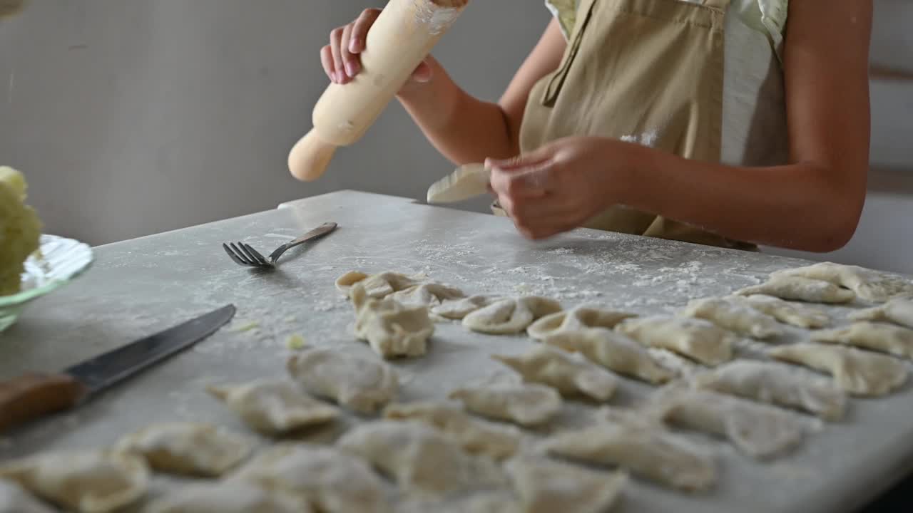 孩子在自家餐桌上用土豆馅做瓦列尼基，展示了用擀面杖和面团准备的传统烹饪过程视频素材