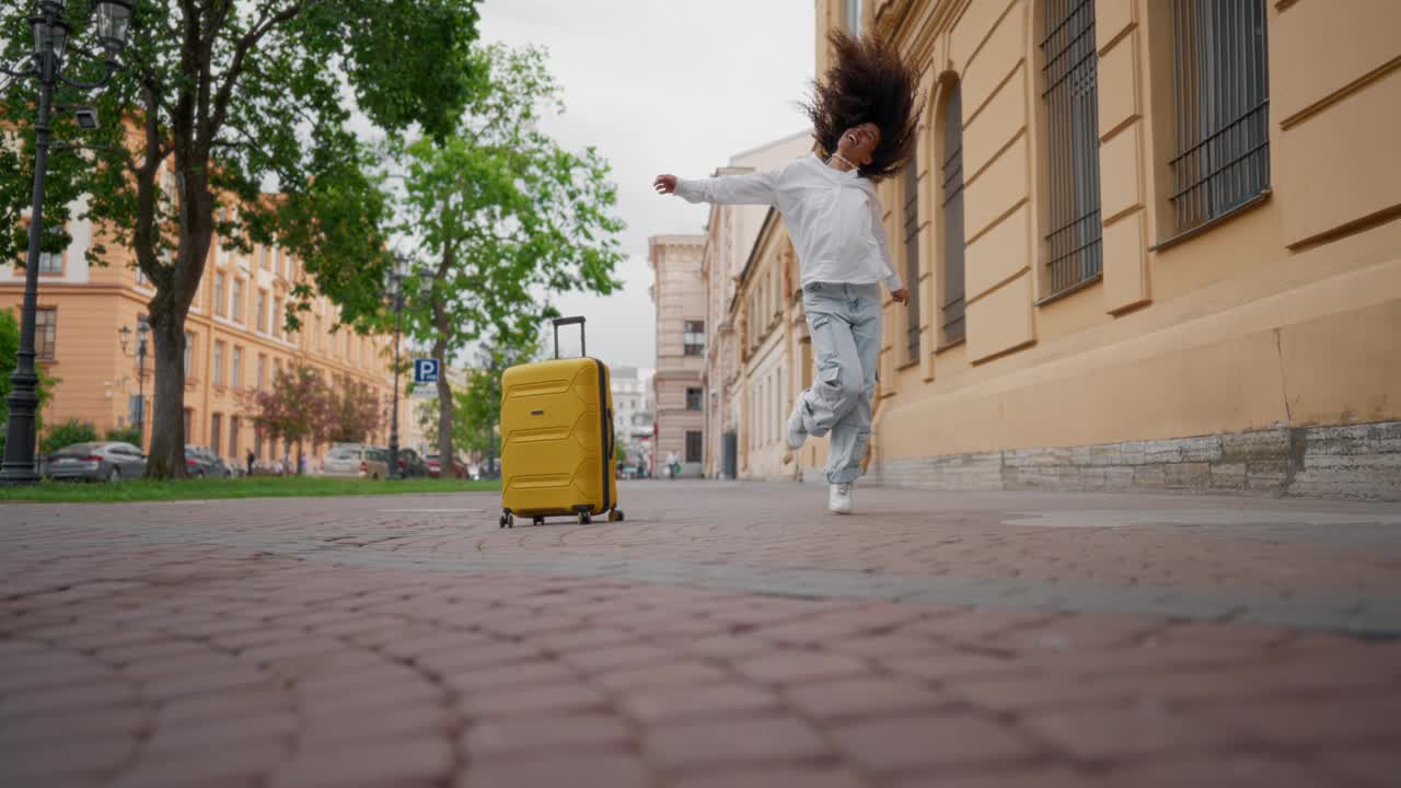 疯狂的混血女人在城市街道上跳舞和跳跃，旅行的乐趣。快乐的非裔美国女游客欢欣鼓舞，表达积极的情绪，全身肖像，慢镜头视频下载