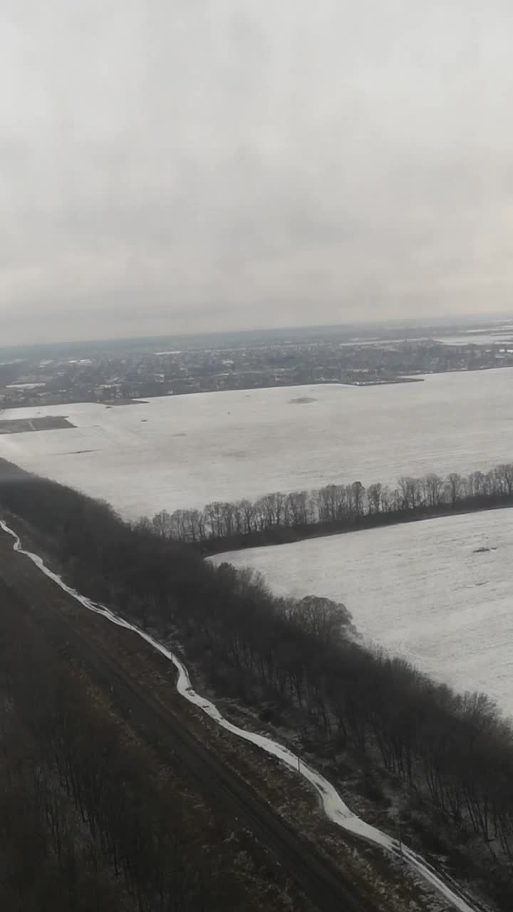 在乌克兰一个灰暗、阴天的冬日，透过飞机的窗户，雨滴展示着白雪覆盖的道路、田野和森林视频下载