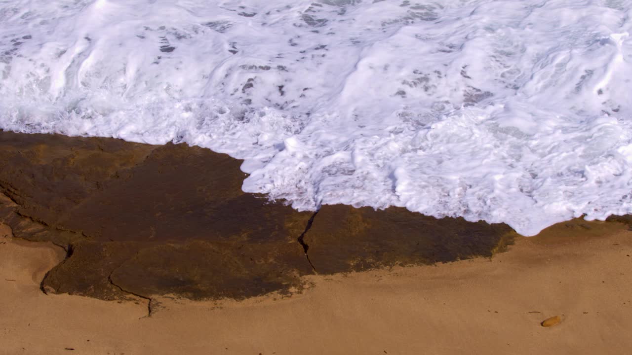 海浪拍打着沙滩上的砂岩礁。视频下载