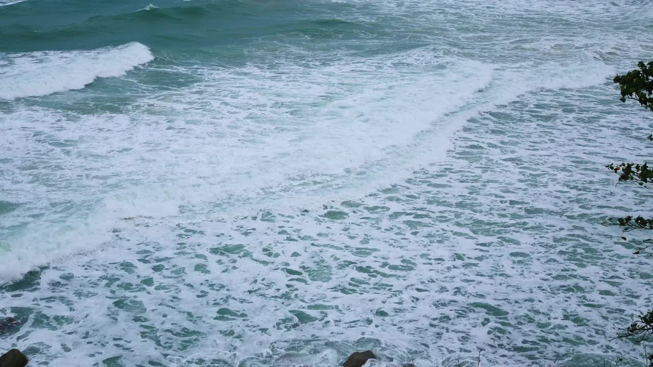 鸟瞰图在大海和岩石悬崖海滩，而绿松石海浪冲击悬崖岩石为夏季旅游假期的背景，从俯视图视频下载