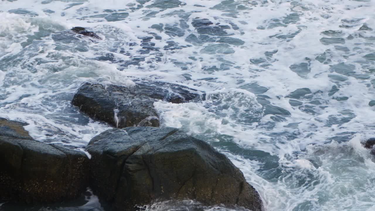 鸟瞰图在大海和岩石悬崖海滩，而绿松石海浪冲击悬崖岩石为夏季旅游假期的背景，从俯视图视频下载