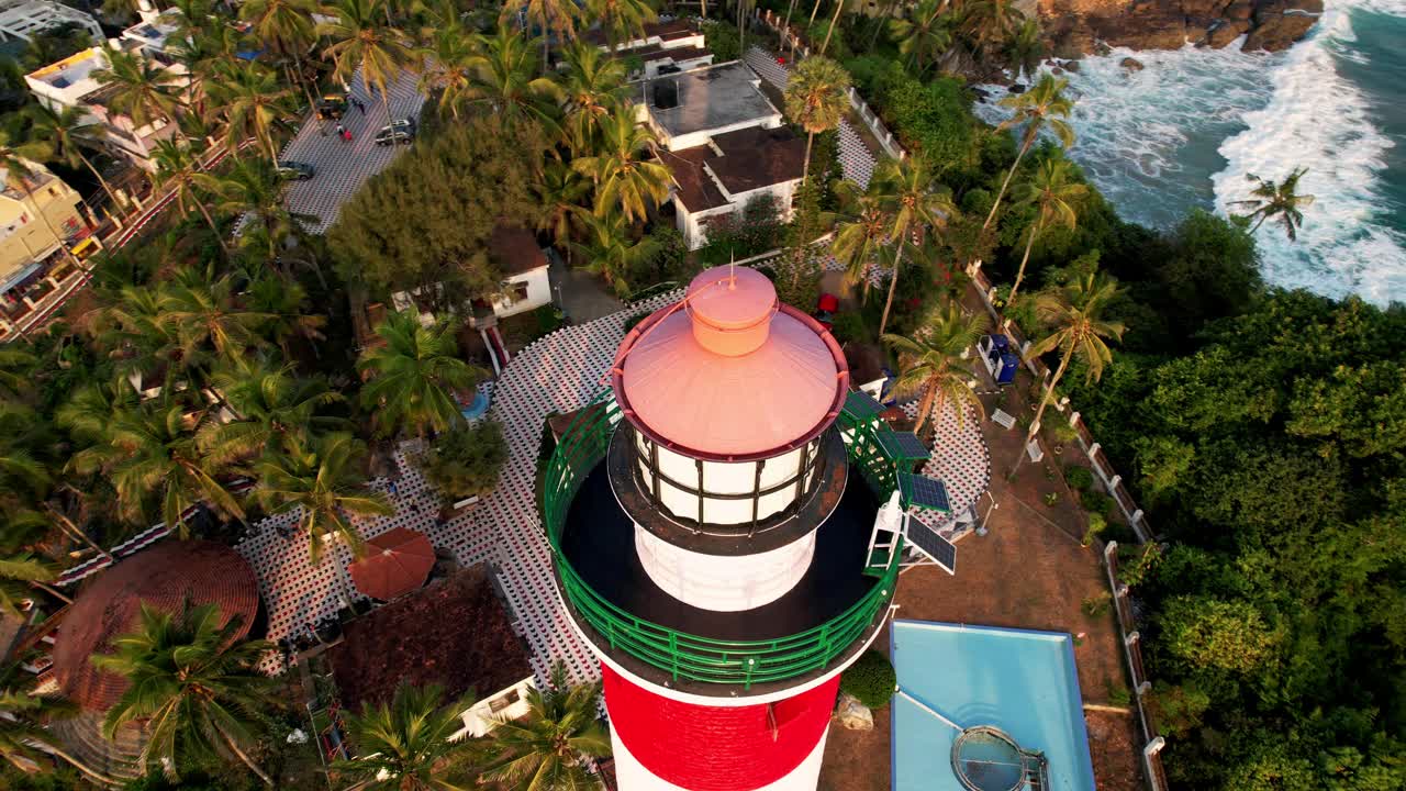 日落时岩石海岸线上的灯塔塔，鸟瞰图。印度喀拉拉邦的Kovalam海滩和灯塔视频下载