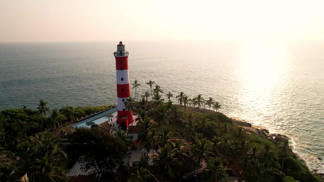 日落时海上海岸线上的灯塔，鸟瞰图。印度喀拉拉邦的Kovalam海滩和灯塔视频下载