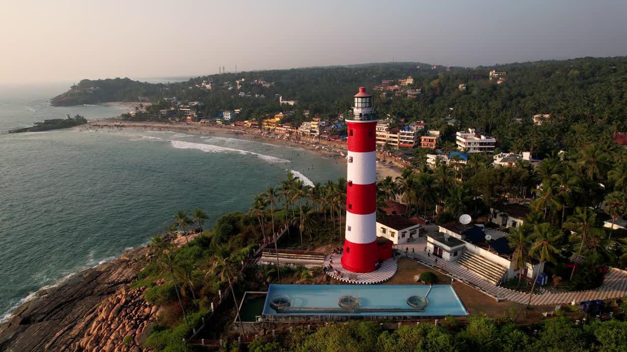 日落时海上海岸线上的灯塔，鸟瞰图。印度喀拉拉邦的Kovalam海滩和灯塔视频下载