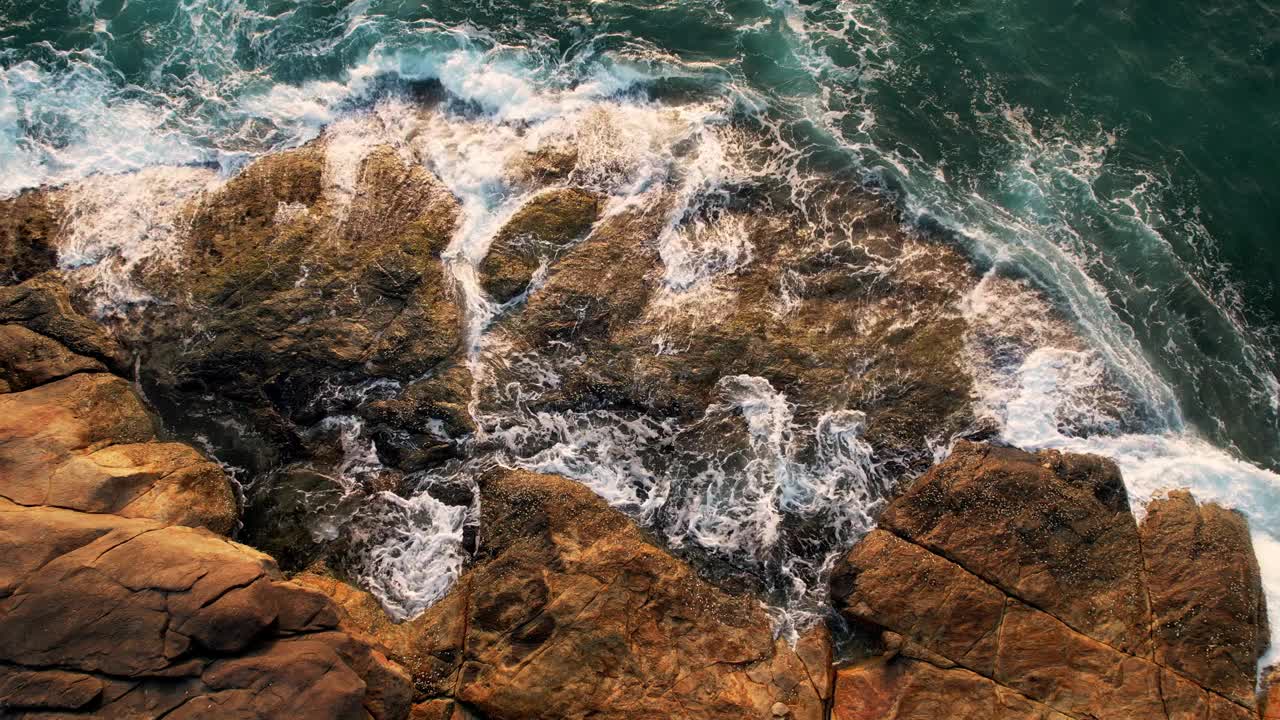 鸟瞰海浪撞击岩石的画面。绿松石般的海浪冲击着岩石般的海岸线，喜怒无常的大海在布满巨石的海岸线周围编织。视频下载