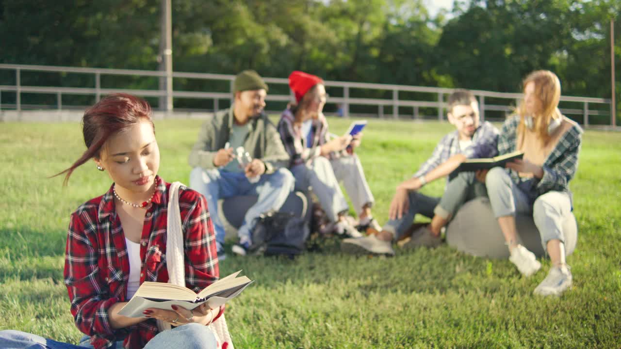 一名身穿红色格子衬衫的亚洲学生，这张照片捕捉到了她在户外学习时，她的同学在后台学习时的专注视频下载