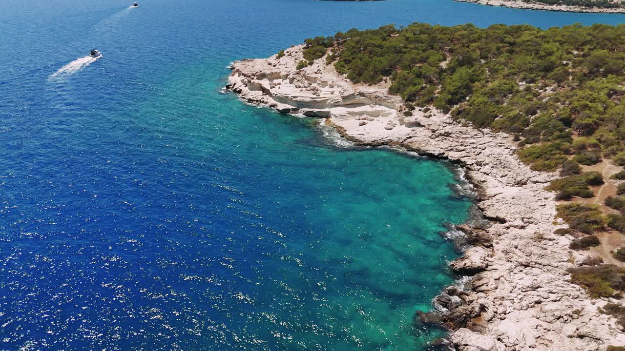 汽艇在碧绿的海水中巡游，沿着美丽的白色悬崖海岸滑行，点缀着郁郁葱葱的绿树，创造出风景如画的海上景色视频素材