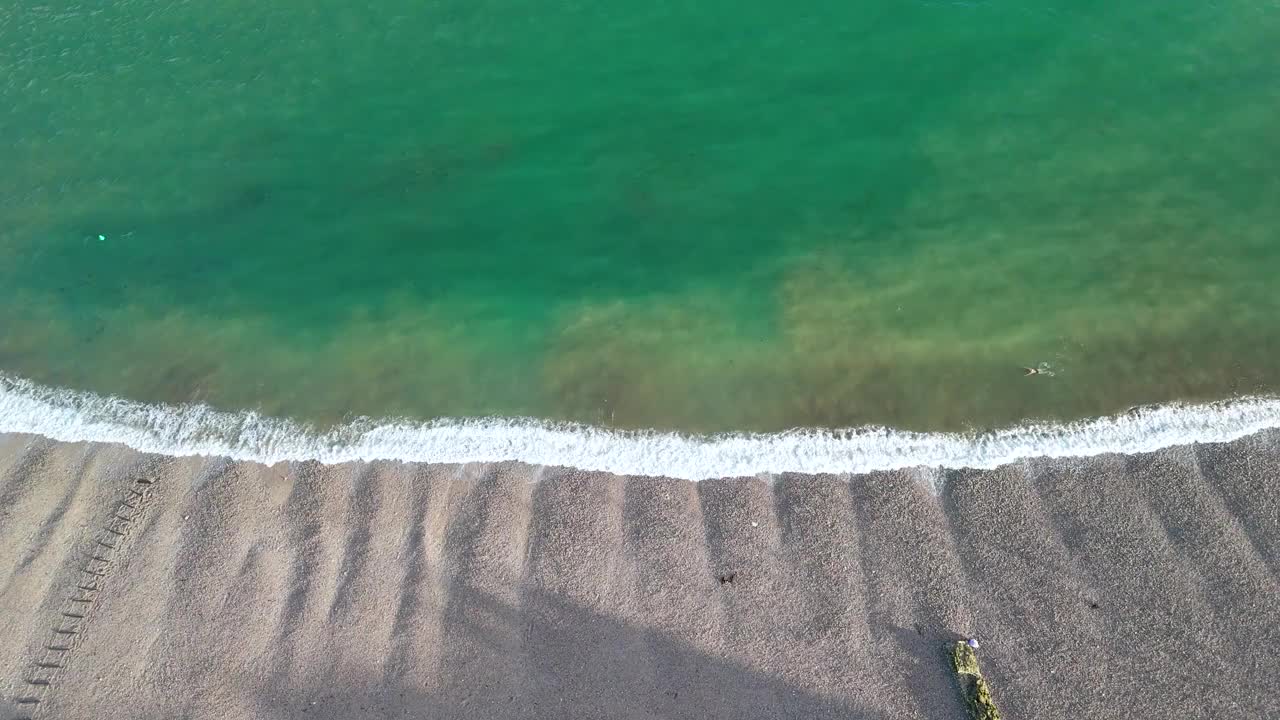 无人机拍摄的海滩上，一个孤独的人沿着海岸游泳。视频下载