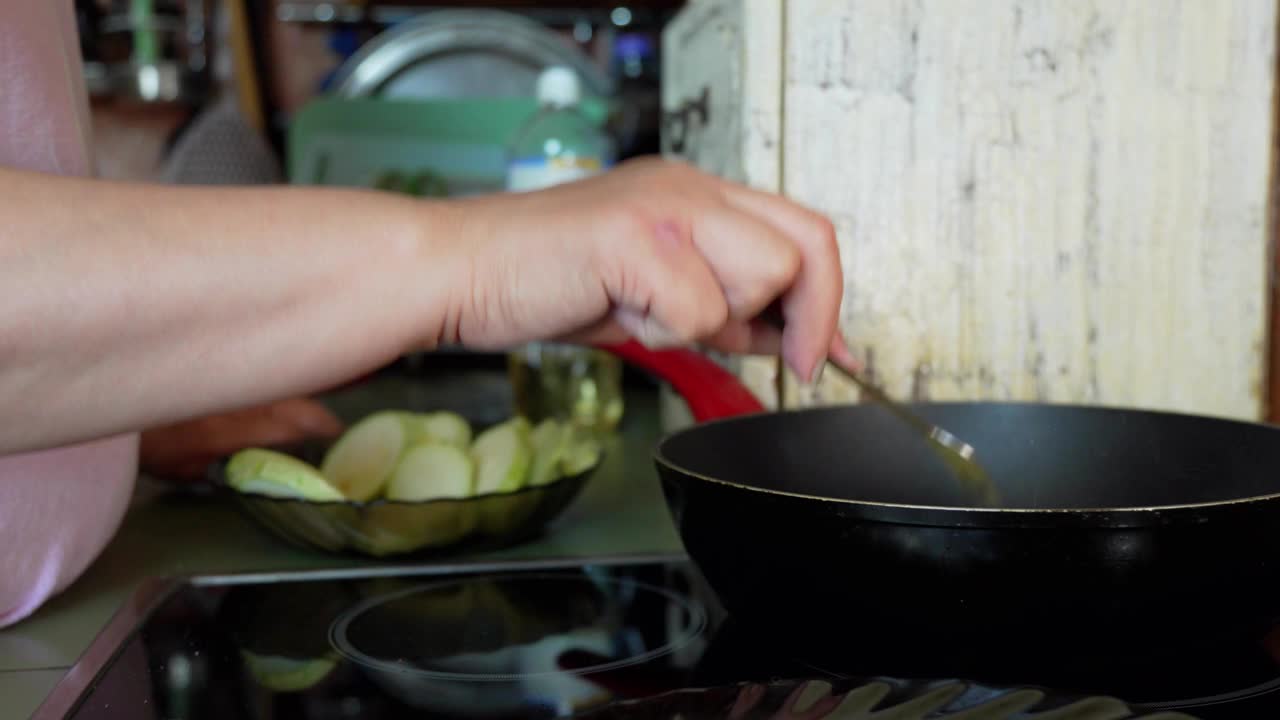 用手小心地往已经在油里滋滋作响的西葫芦片锅里加入调味料。视频素材