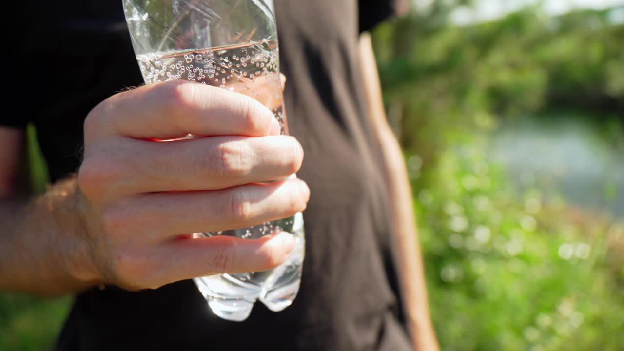 一名身穿黑色t恤的男子右手拿着一个透明的塑料水瓶。视频素材