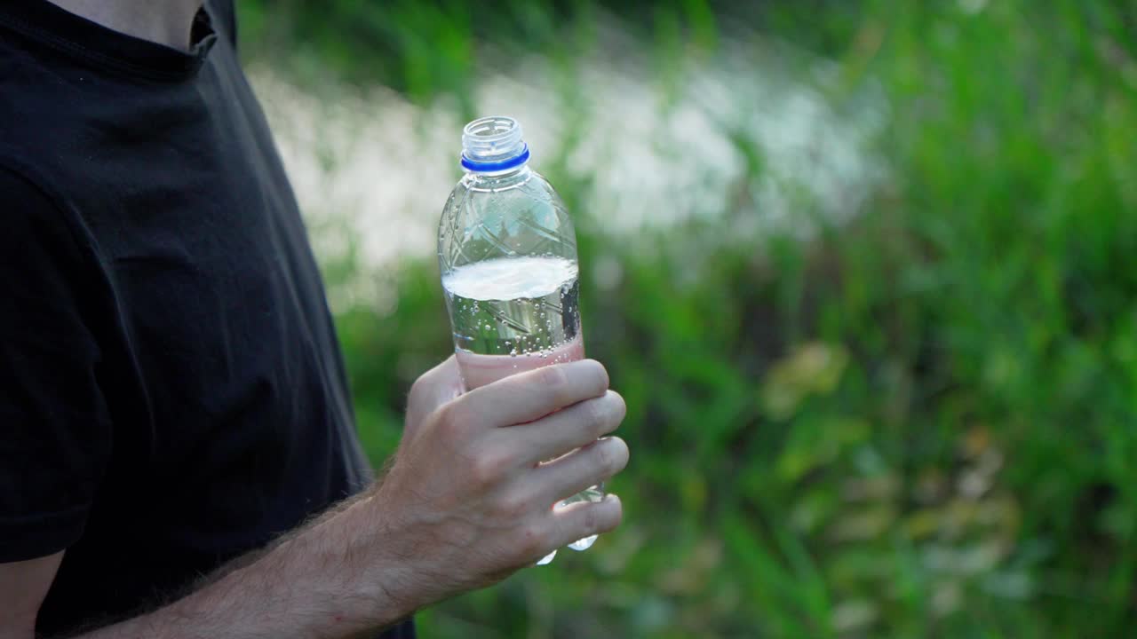 郁郁葱葱的绿色植被环绕着他，他右手拿着一个深色的水瓶视频下载