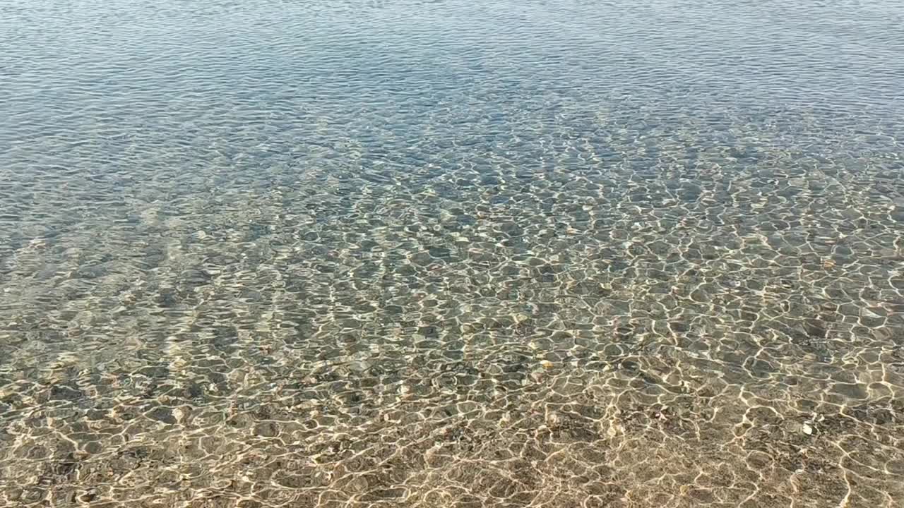 自然平静的大海背景。闪闪发光的海水和金色的沙子。夏日热带海滩上的海浪。阳光反射在水面上。浅浅的海水泛起涟漪。海床上的阳光。视频素材