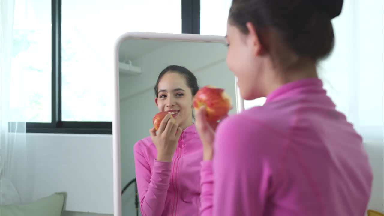 一位身穿粉色运动服的芭蕾舞女学生在练习芭蕾舞前吃了一个苹果视频下载